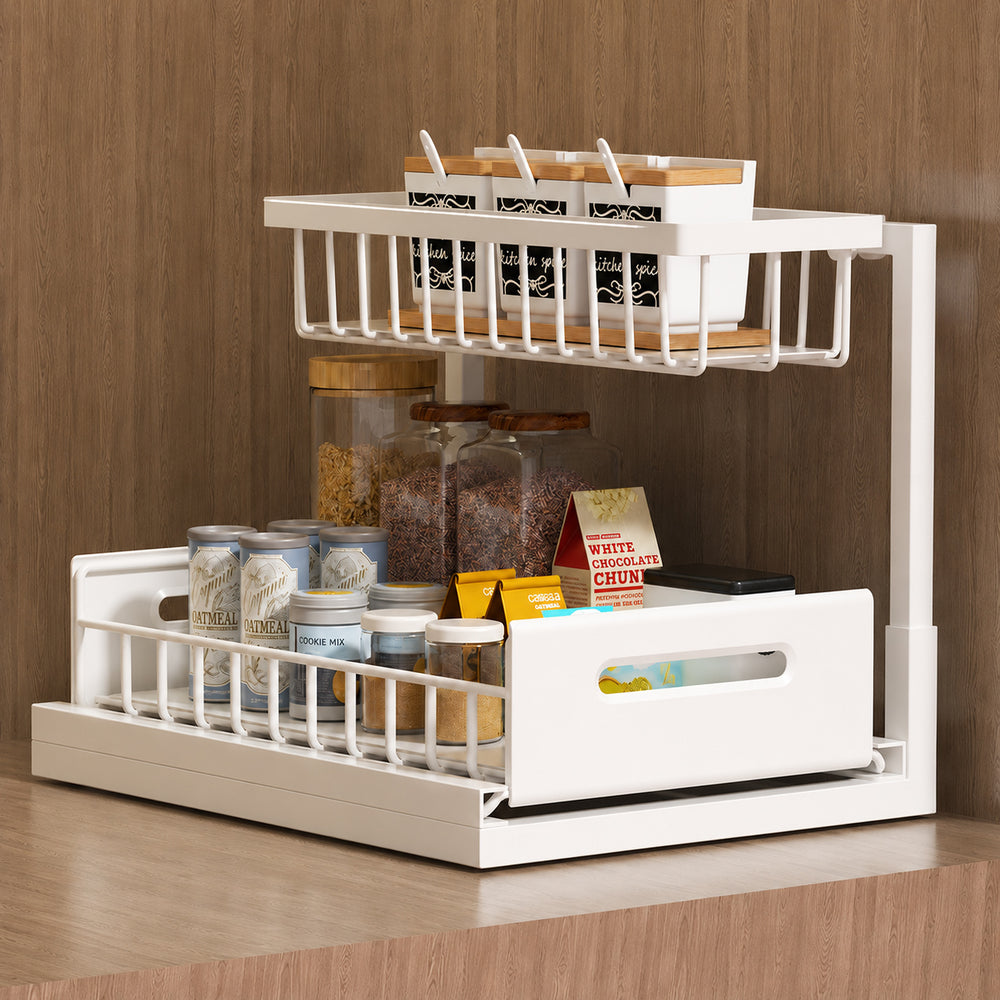 A white two-tier kitchen spice rack organizer filled with glass jars, spice boxes, and containers, set against a wood-paneled background.